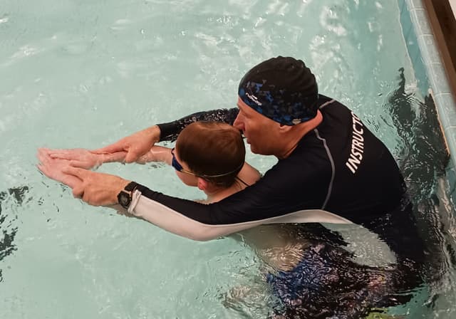 Swim coach Vladimir helping a kid with his breast stroke